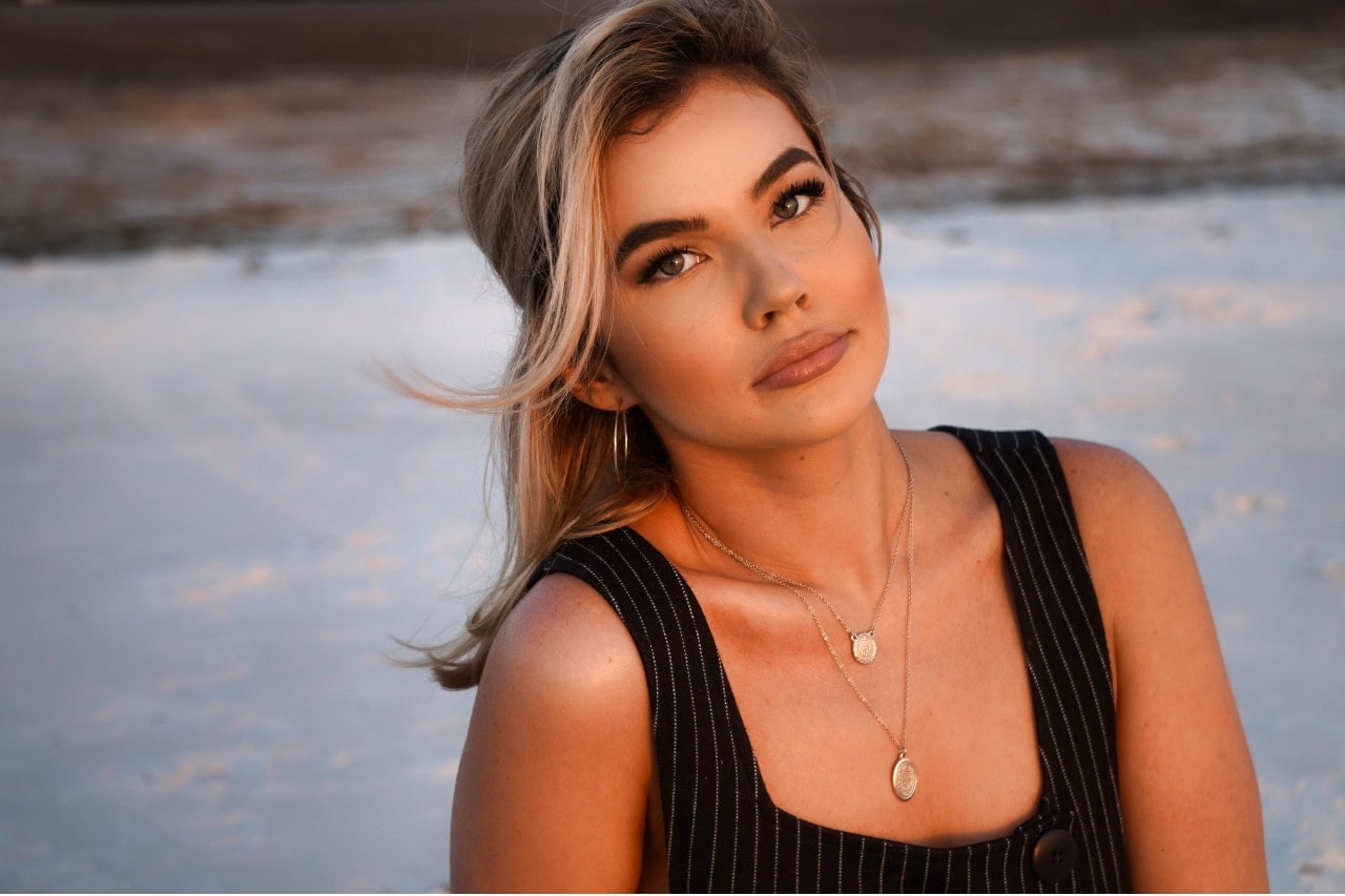 A woman watching the sunset with two gold medallion necklaces on