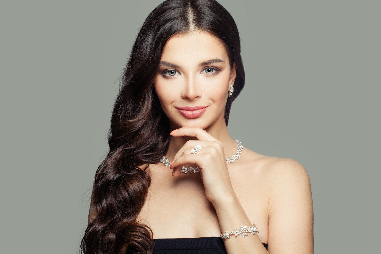 A woman wearing a matching set of floral and diamond motif bracelet, fashion ring, collar necklace, and earrings