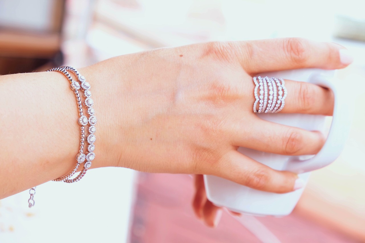 A woman holding a coffee cup wearing an intricate band design detailed with many tiny diamonds and two diamond bracelets