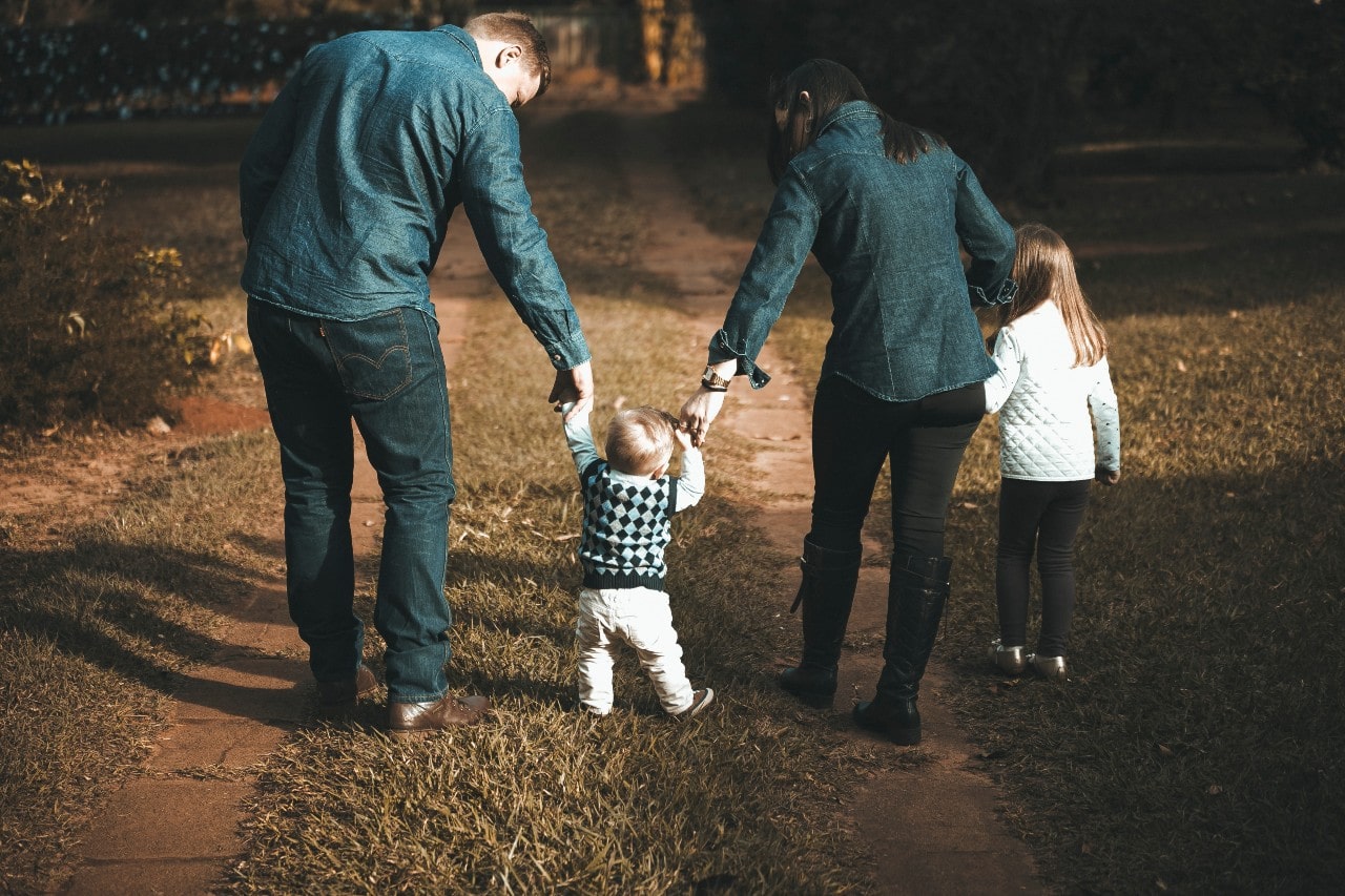A young family holds hands and walks along a driveway