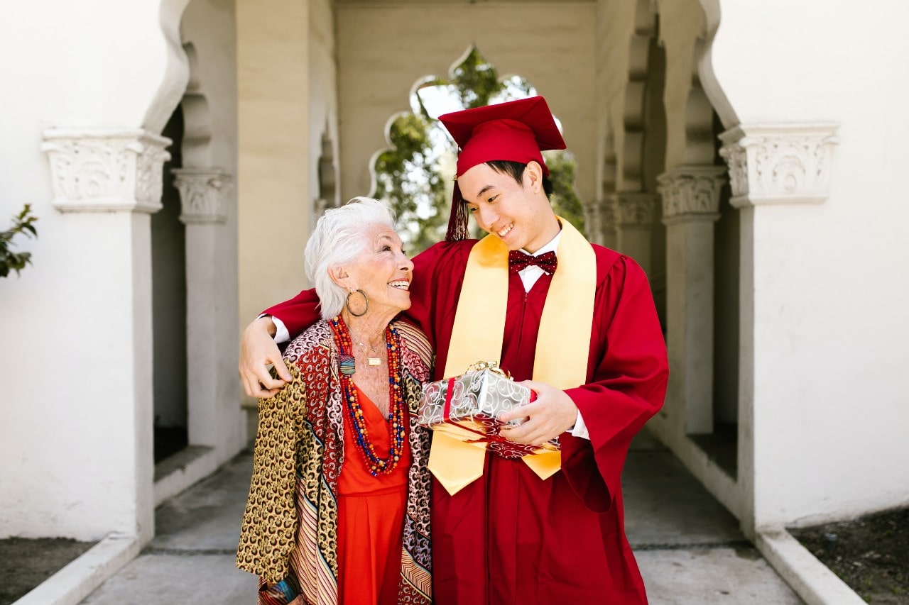 A college graduate hugs his grandma while holding his wrapped graduation gift