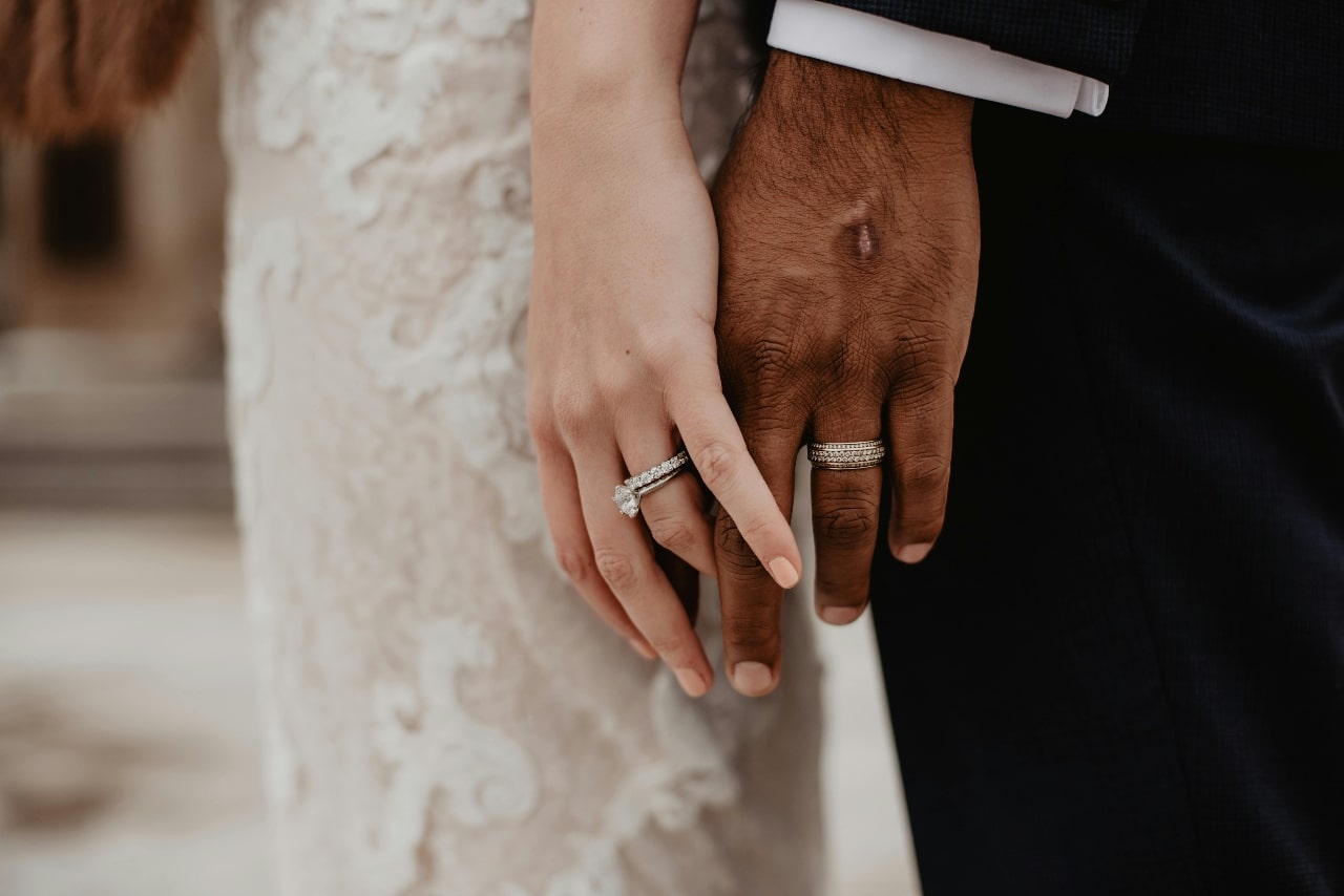 Two hands adorned with wedding and engagement rings, showcasing the union of a couple in formal attire