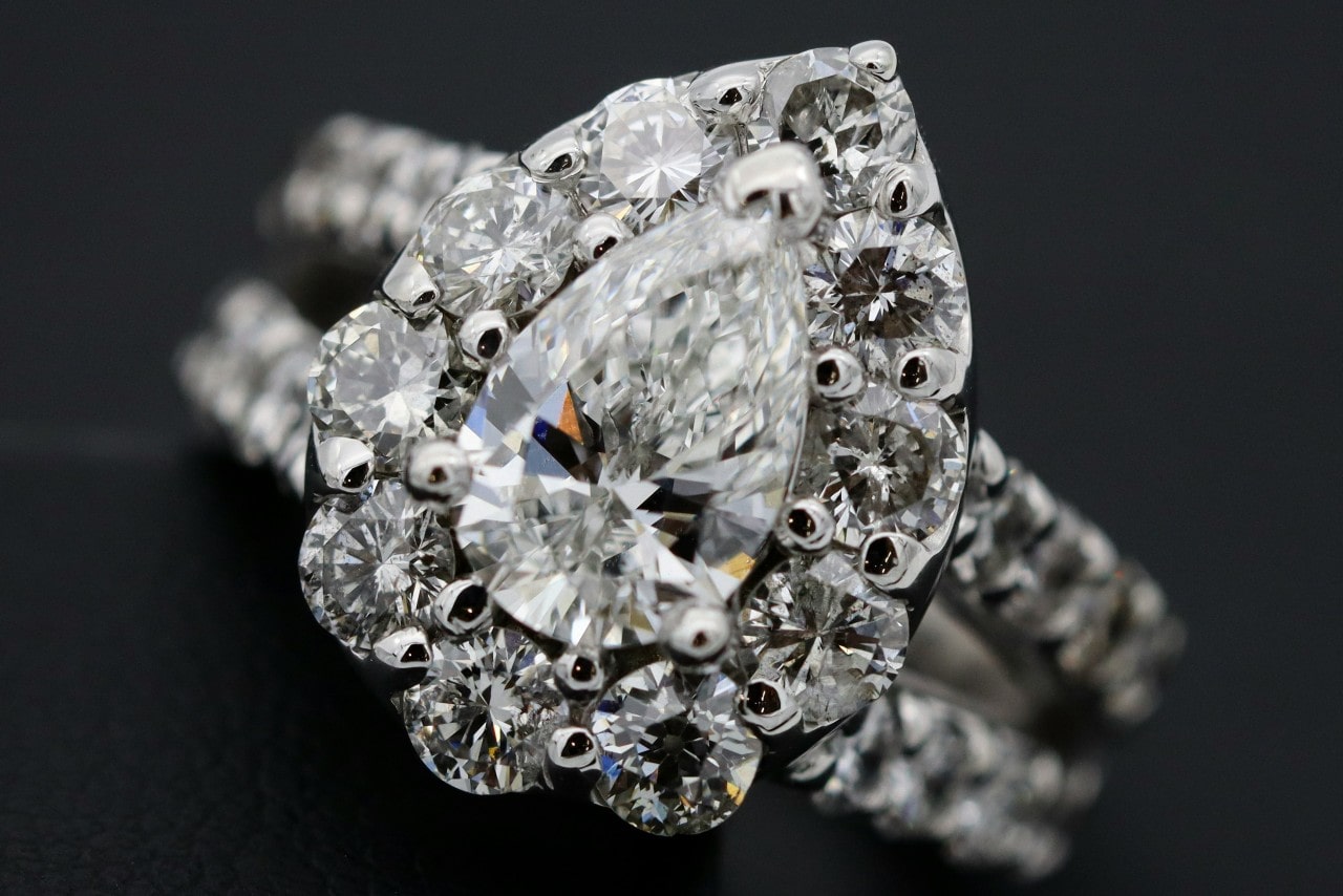 A pear-shaped diamond ring surrounded by smaller round diamonds on a silver band, set against a black background.