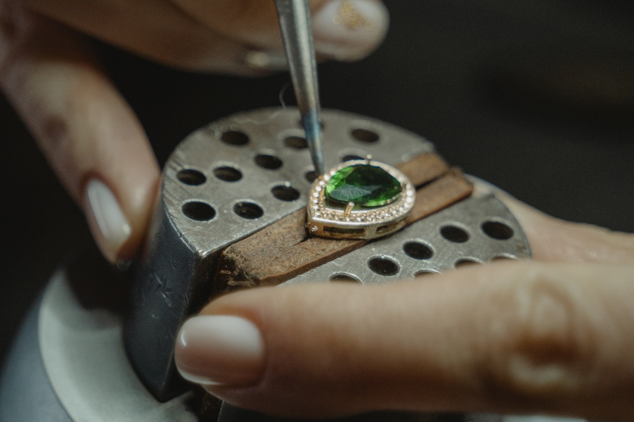 A close-up of a jeweller working on a piece with a green pear cut centre stone. A close-up of a jeweller working on a piece with a green pear cut centre stone.