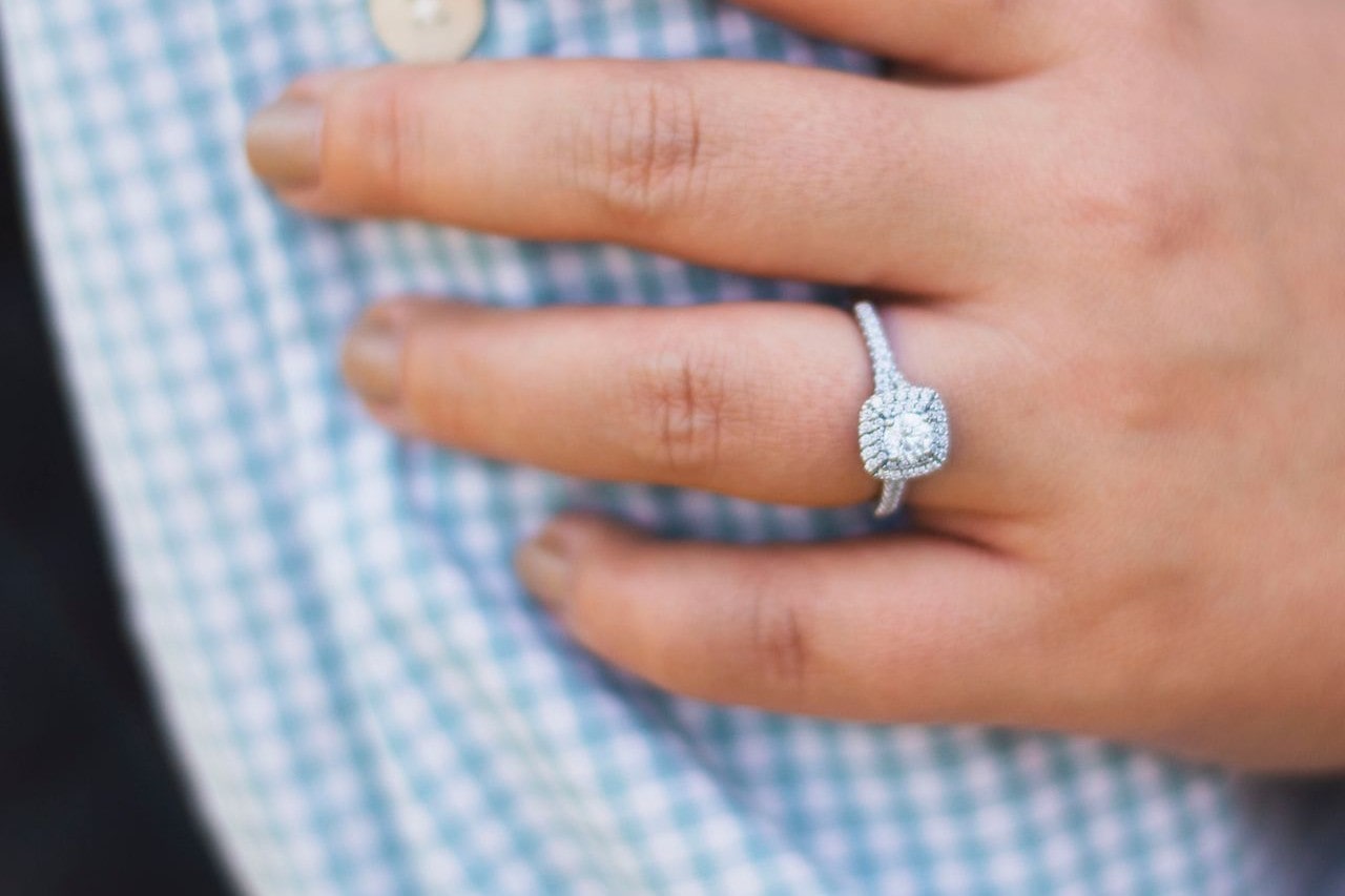 diamond halo engagement ring on finger on blue plaid shirt